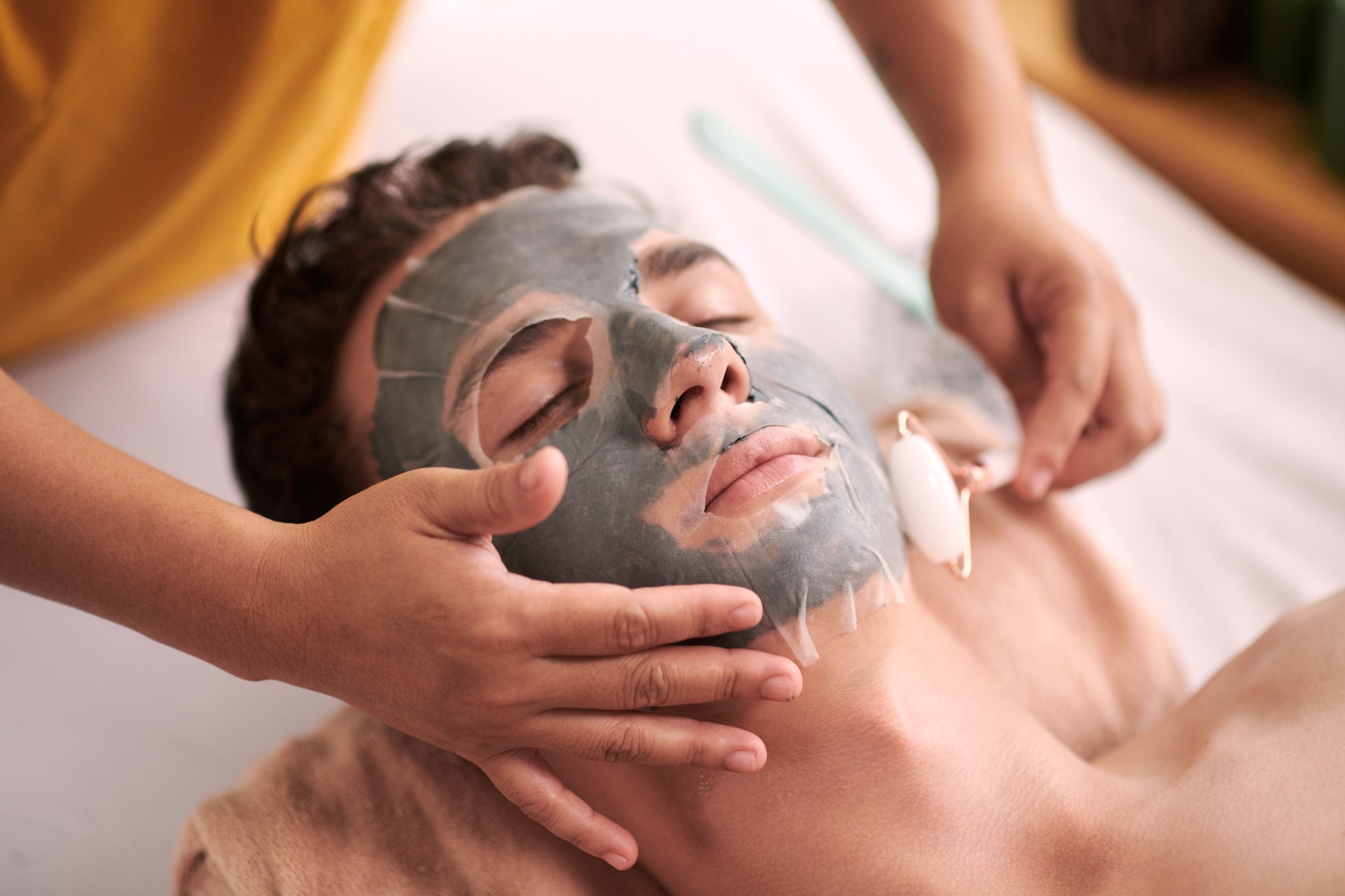 Hand of female beautician touching face of young male client with sheet mask