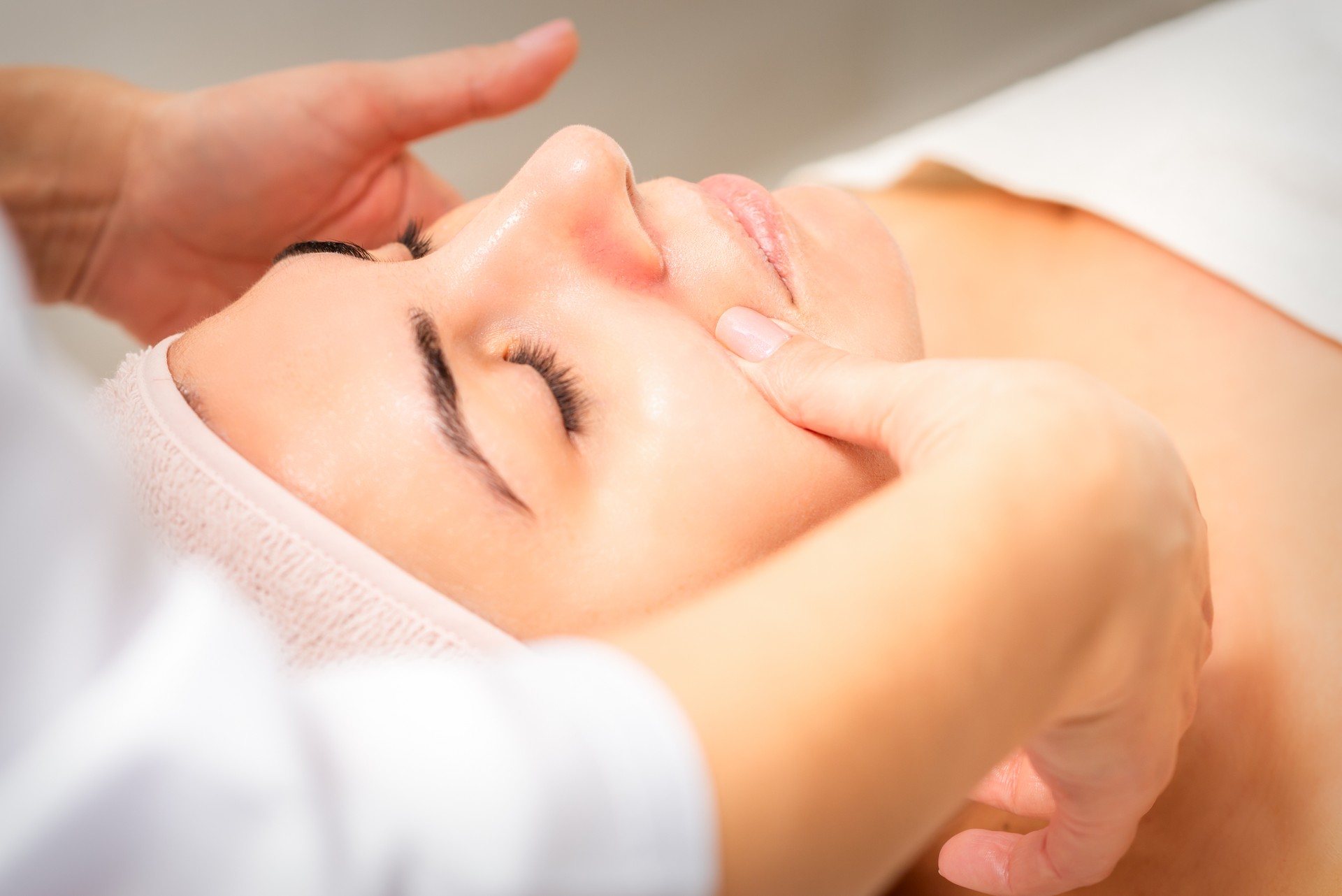 Beautician making lymphatic drainage face massage or facelifting massage at the beauty salon.